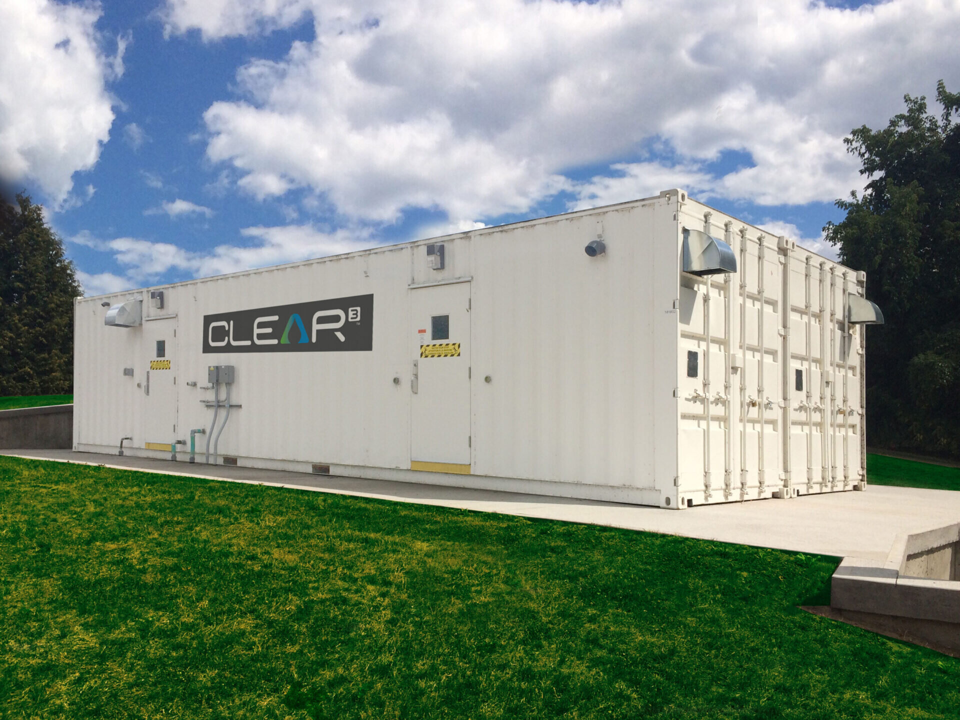 ANewterra Clear3 decentralized membrane bioreactor consisting of a white shipping container with locking doors and branded with the Clear3 logo on a concrete slab in an outdoor setting with green grass and blue skies