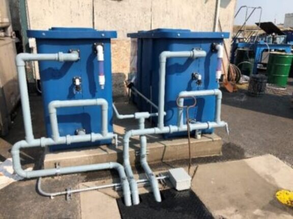 Two large plastic of metal containers installed on a concrete slab at a boatyard filter water through a series of pipes after the contaminated storm water is filtered by gravity to remove zinc and copper contaminants