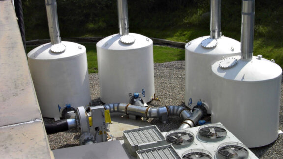 Four Newterra filters sit outside an industrial site with large pipes entering each filter vessel with a valve wheel