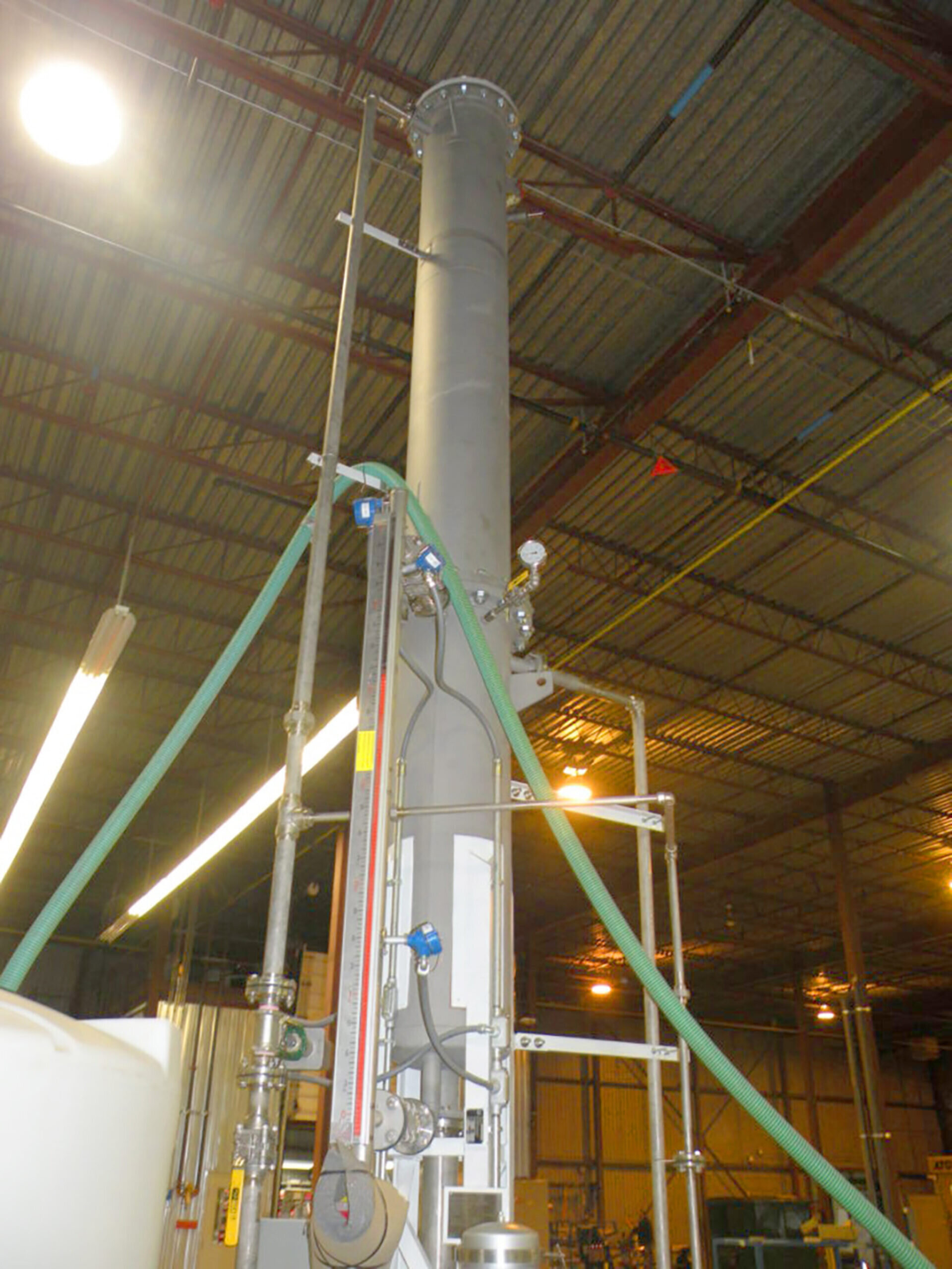 A vacuum dearator using forced air degassifiers in an industrial warehouse consisting of a large metal or concrete tube with a pressure or temperature gauge, hoses, and lever valves.