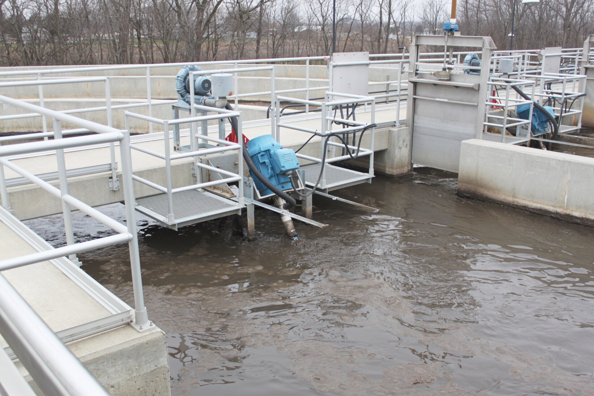 A concrete open containment pond with service walkways and metal platforms support the Newterra Triton 2.0 process aerator mixer with a bridge mount; water moves as the unit mixes the treatment water