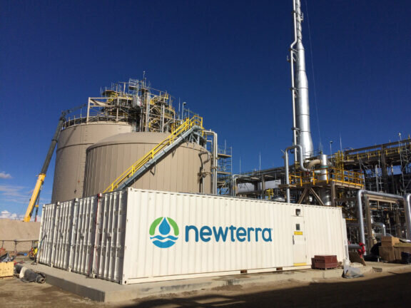 Four Newterra water treatment units sit side by side on a concrete slab at a oil and gas refinery