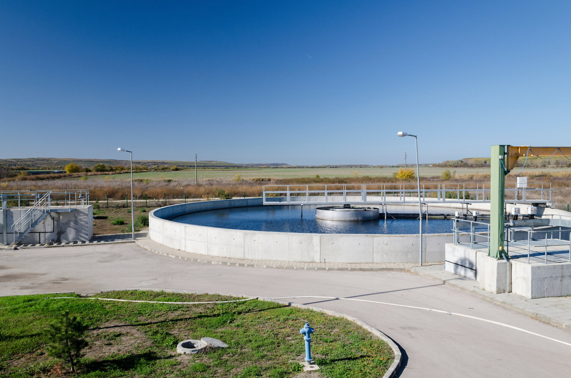 A large pond holding tank containing cleaned water in a rural area with concrete sidewalks around the tank