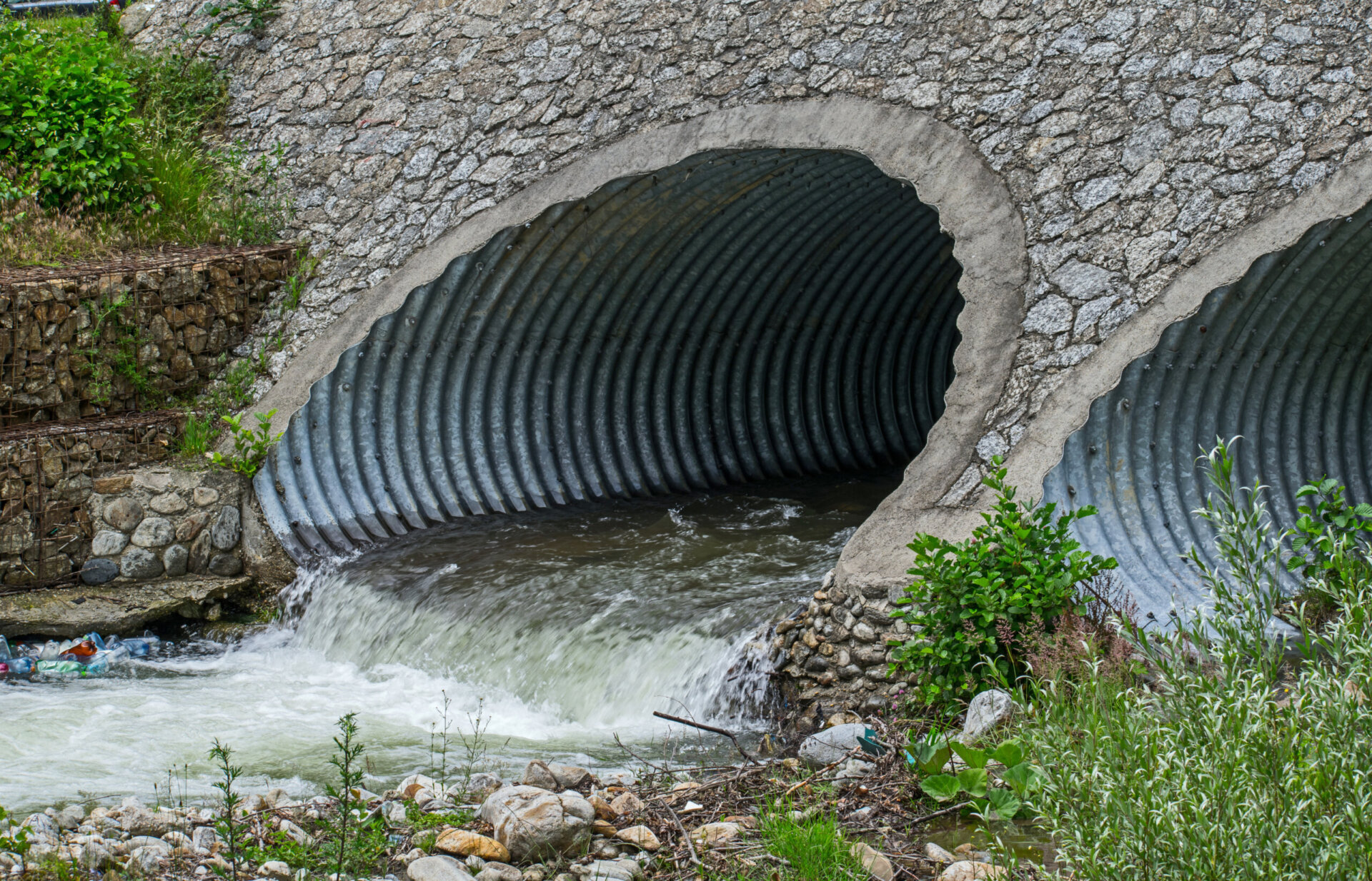 Water drains through pipes, under a bridge.