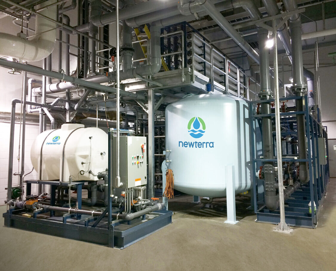 Industrial water treatment technology inside a building featuring metal and plastic tanks with pipes extending in many directions with walking platform over the tanks