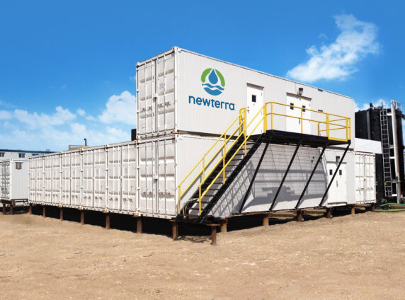 Five modular containers arranged four on lowest level and one stacked on the container closest to the photographer with black steel staircase with yellow guard rail leading to three doors in the top level container outdoors.