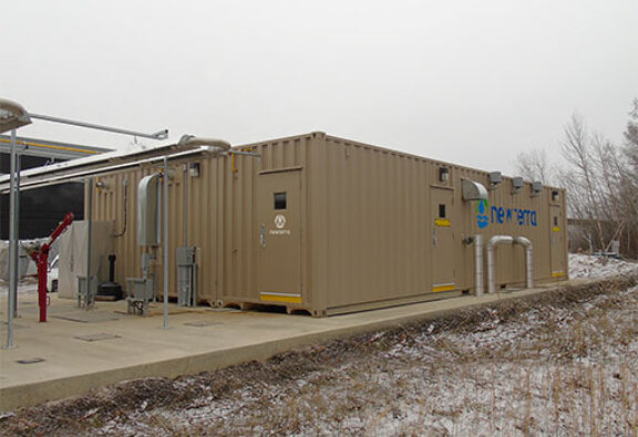 Colorado wastewater project in McDonald Island and MBR unit outdoors consisting of a corrugated metal tan building with various steel pipes exiting or entering the structure into the surface below the concrete slab foundation