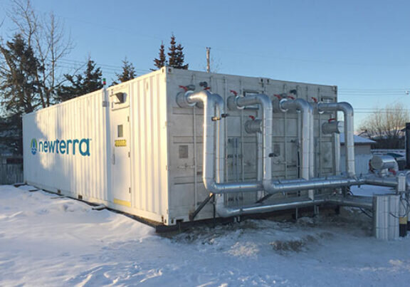 Newterra goundwater remediation system contained in two shipping containers with multiple steel tubes connecting to additional external tubes in a snowy environment with trees