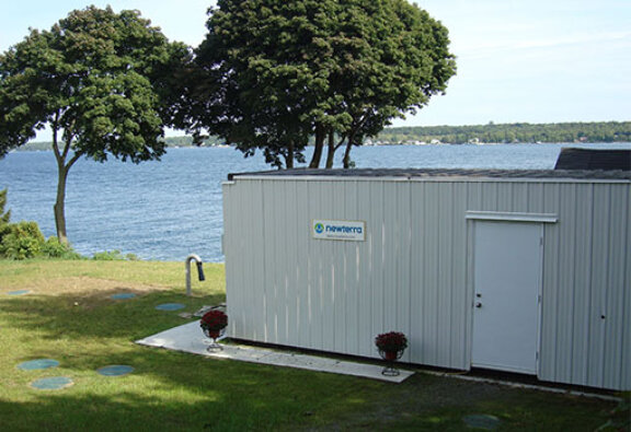 Newterra decentralized modular MBR treatment container placed near a river with trees, upland shoreline in the background on opposite side of river