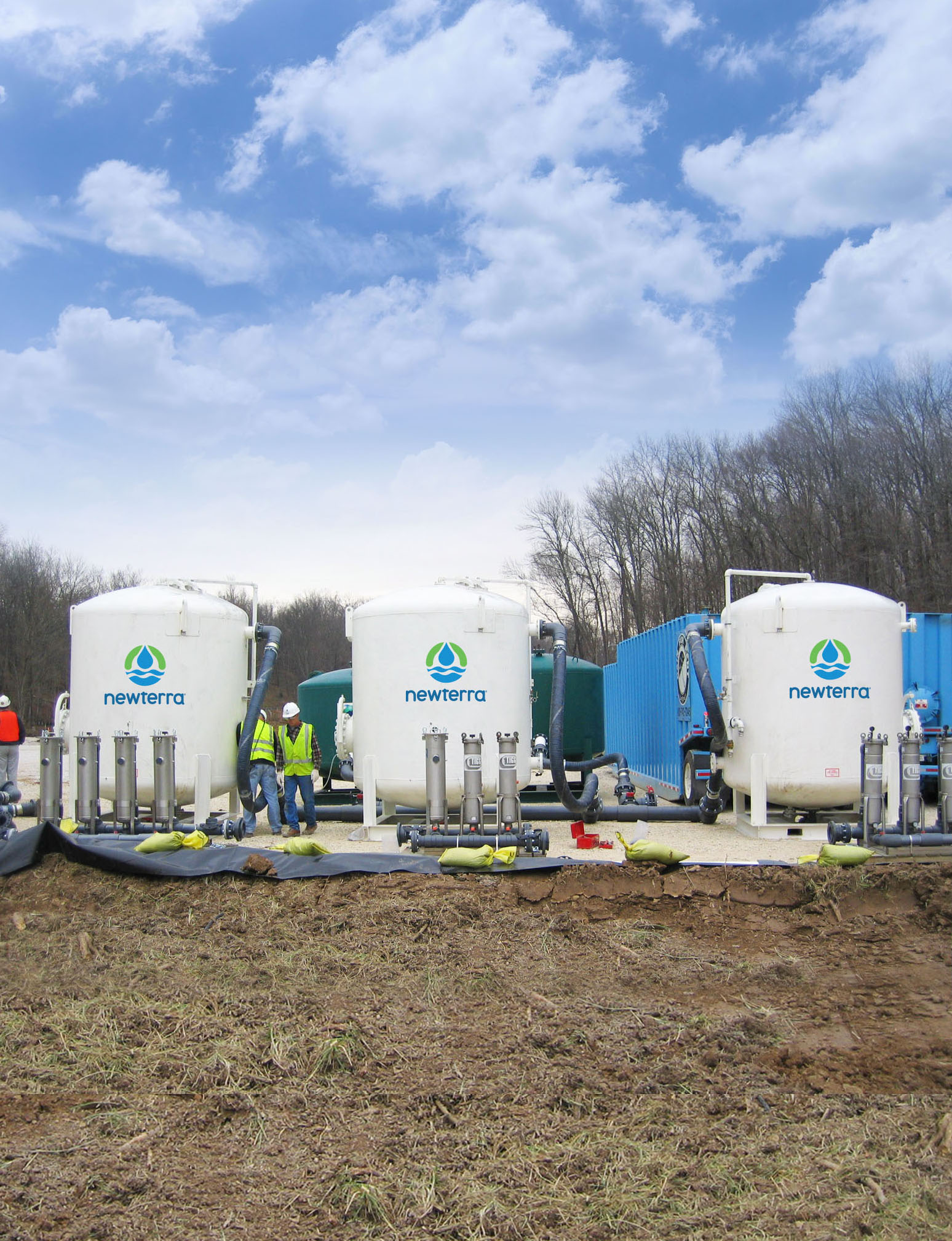 Three technicians inspect three Newterra branded tanks used for treating wastewater in an outdoor setting surrounded by trees