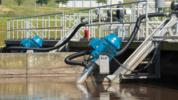 2 Newterra Tritons half submerged in the water at a treatment facility with green grass in background